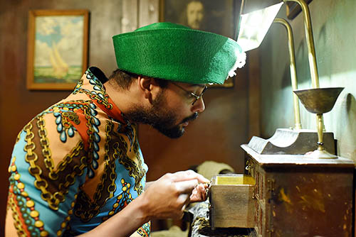 Man in green hat peeking in a tiny drawer in the Mardi Gras Study