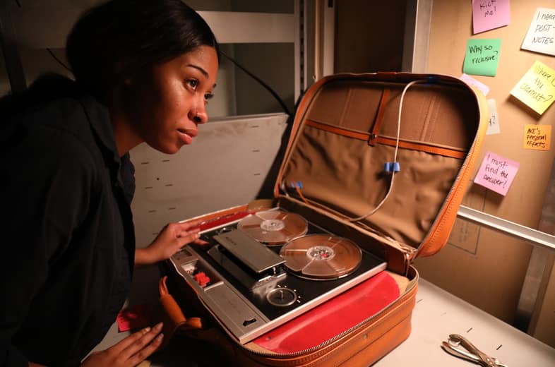 Player examining a vintage reel-to-reel tape recorder for clues